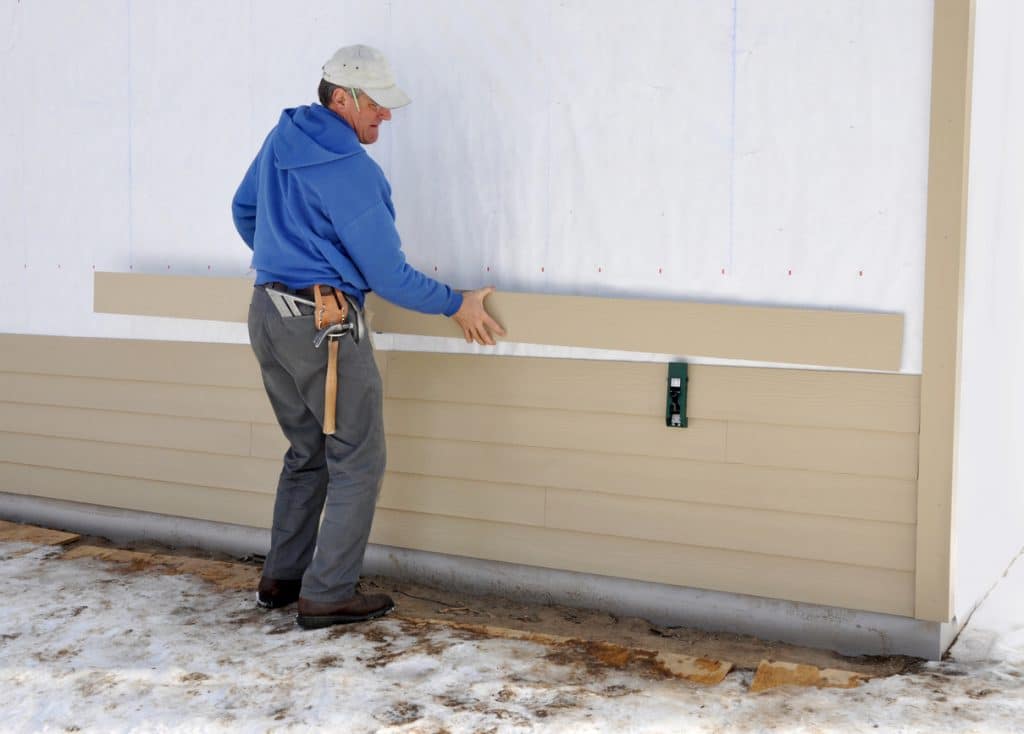 A man in blue jacket holding a pipe next to a wall.